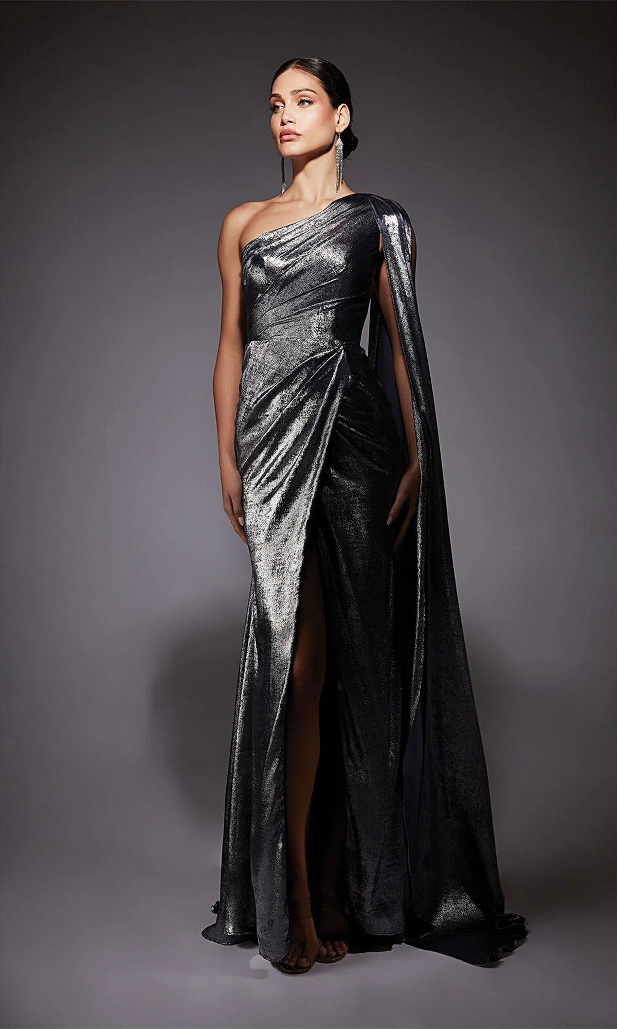 A woman poses in the Alyce 27753 long formal dress, a metallic silver chiffon one-shoulder evening gown with a thigh-high slit and draped fabric, set against a plain dark background.